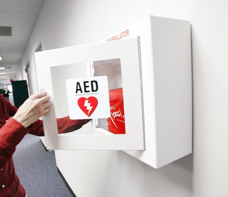 hand reaches into an AED case mounted on a wall