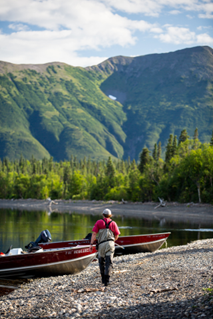 researcher conducts fieldwork near a lake with mountains in background